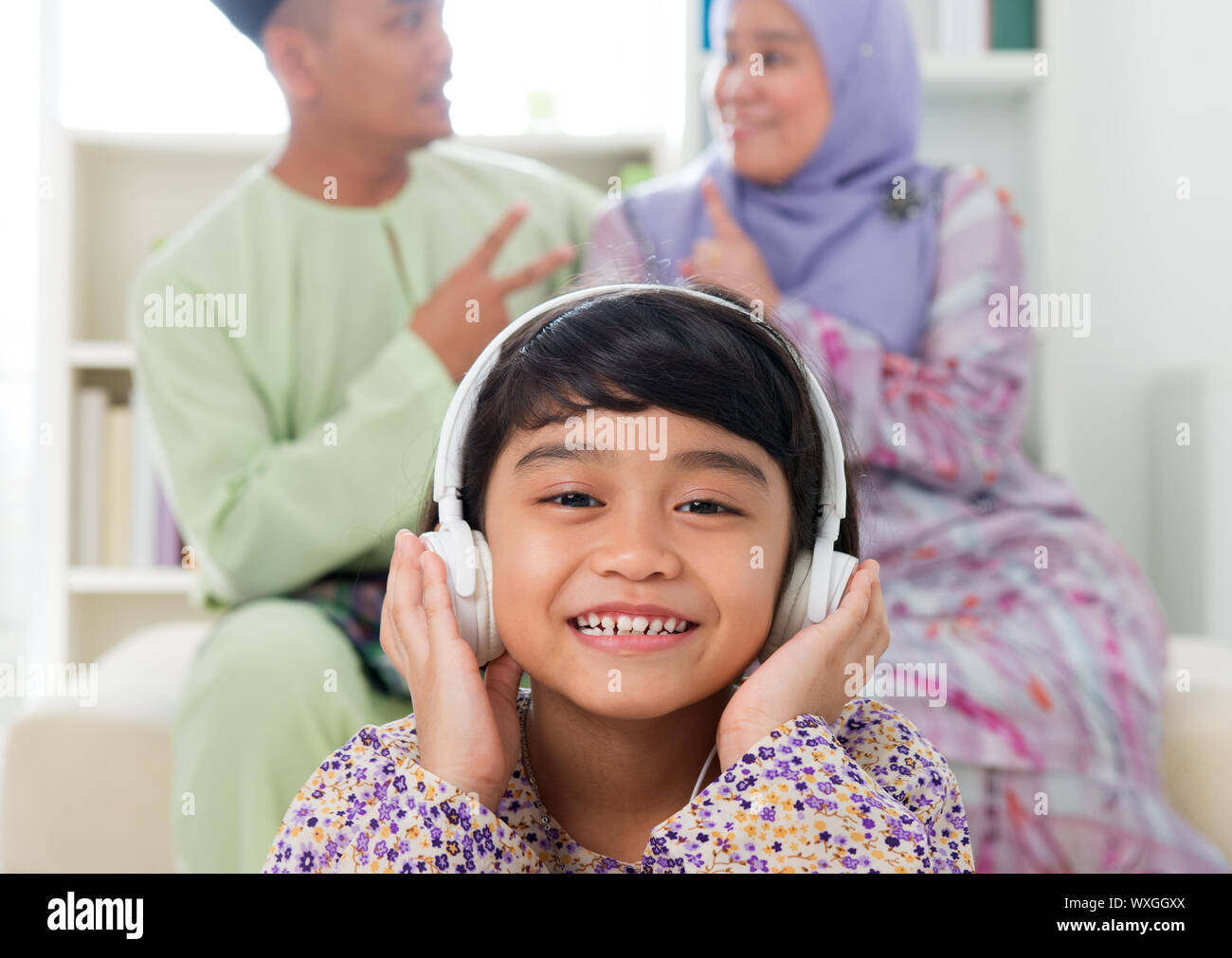 Ragazzina musulmana ascoltando la canzone a casa. Sud-est asiatico vivere in famiglia stile di vita. Sorridenti Malay i genitori e il bambino. Foto Stock