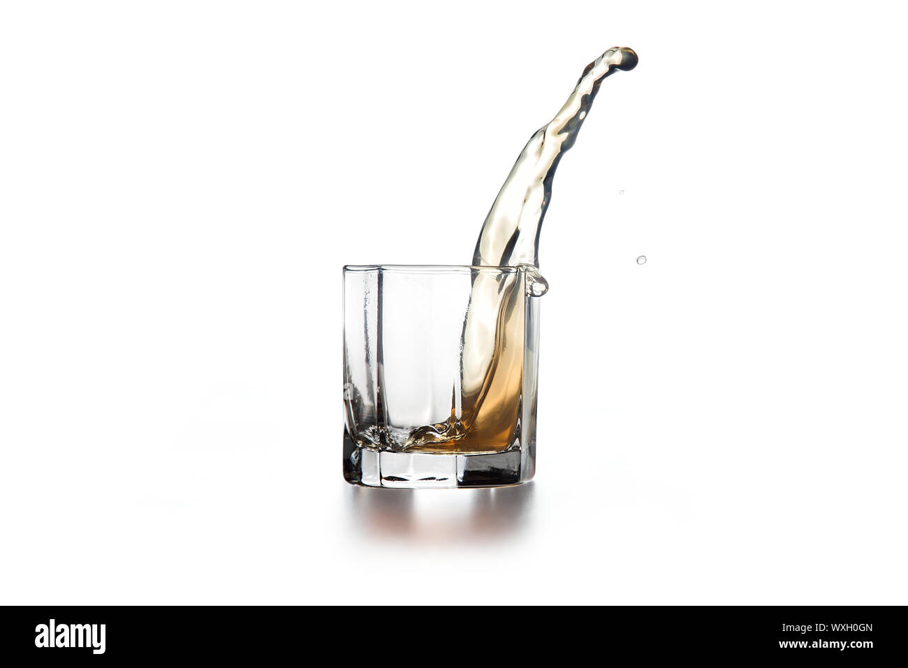 Whiskey splash di vetro, con tante gocce di bevanda uscire dal vetro su sfondo chiaro. Foto Stock