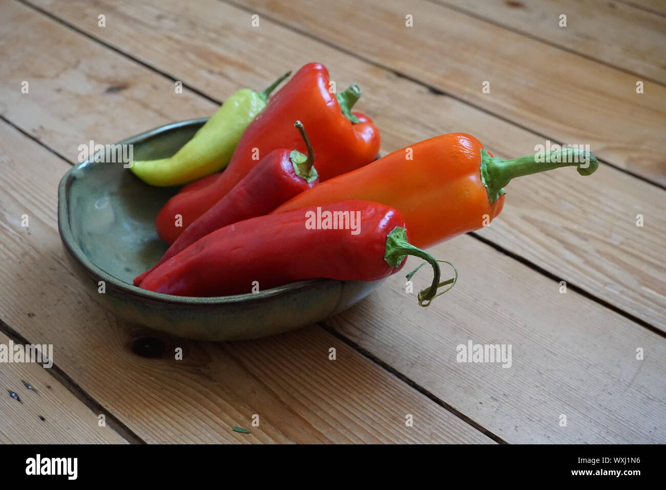 Assortimento di variopinte i peperoni in un piatto di ceramica su una tavola in legno rustico Foto Stock