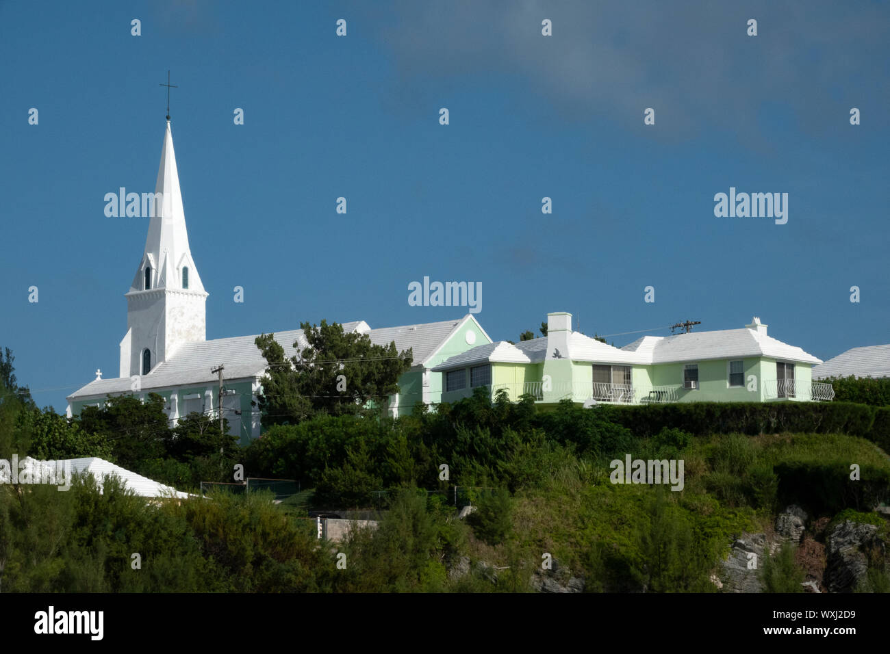 Un dipinto di bianco chiesa in Bermuda contro un cielo blu con vegetazione in primo piano Foto Stock