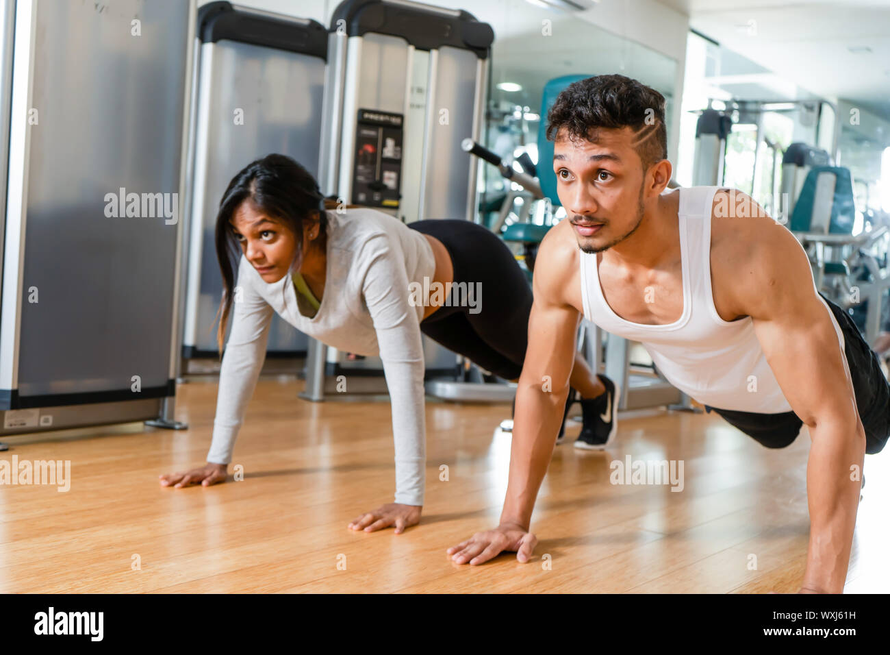 Allegro coppia giovane esercizio avambraccio plank fianco a fianco su stuoie durante l'allenamento all'interno di un moderno fitness club Foto Stock