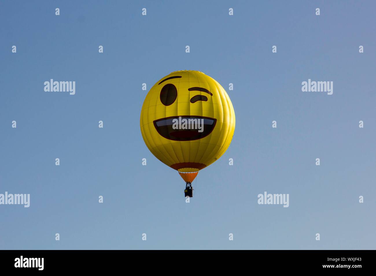 Un giallo, felice occhiolino gli Emoji mongolfiera volare contro un cielo blu. Smile. 2 Foto Stock