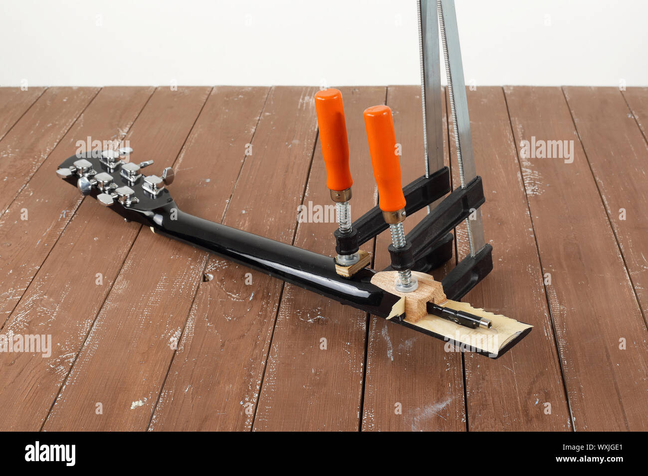 La riparazione di una chitarra e il servizio di assistenza - il serraggio di una chitarra di legno del collo e sfondo bianco Foto Stock