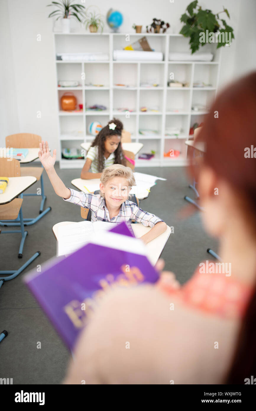 Scolaro alzando la mano mentre avente risposta per insegnante Foto Stock