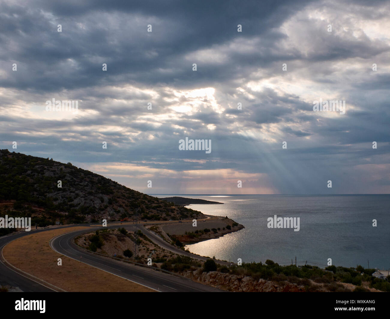 Raggi di sole rompere attraverso le nuvole alla superficie del mare. Strada tortuosa in mattinata. Foto Stock