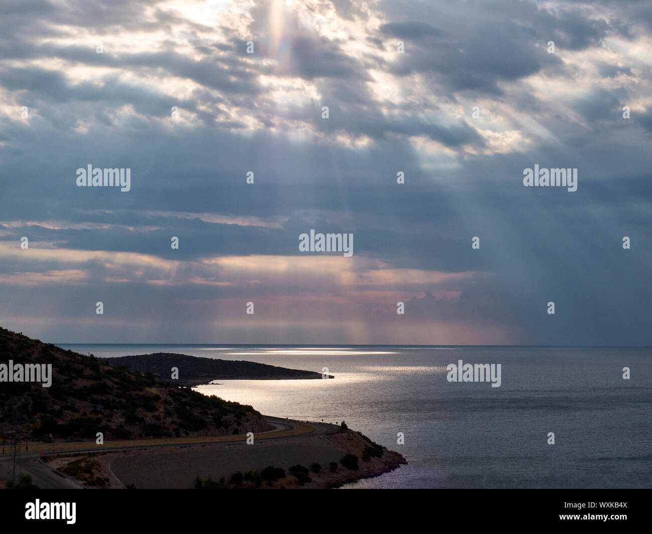 Raggi di sole rompere attraverso le nuvole alla superficie del mare. Strada tortuosa in mattinata. Foto Stock