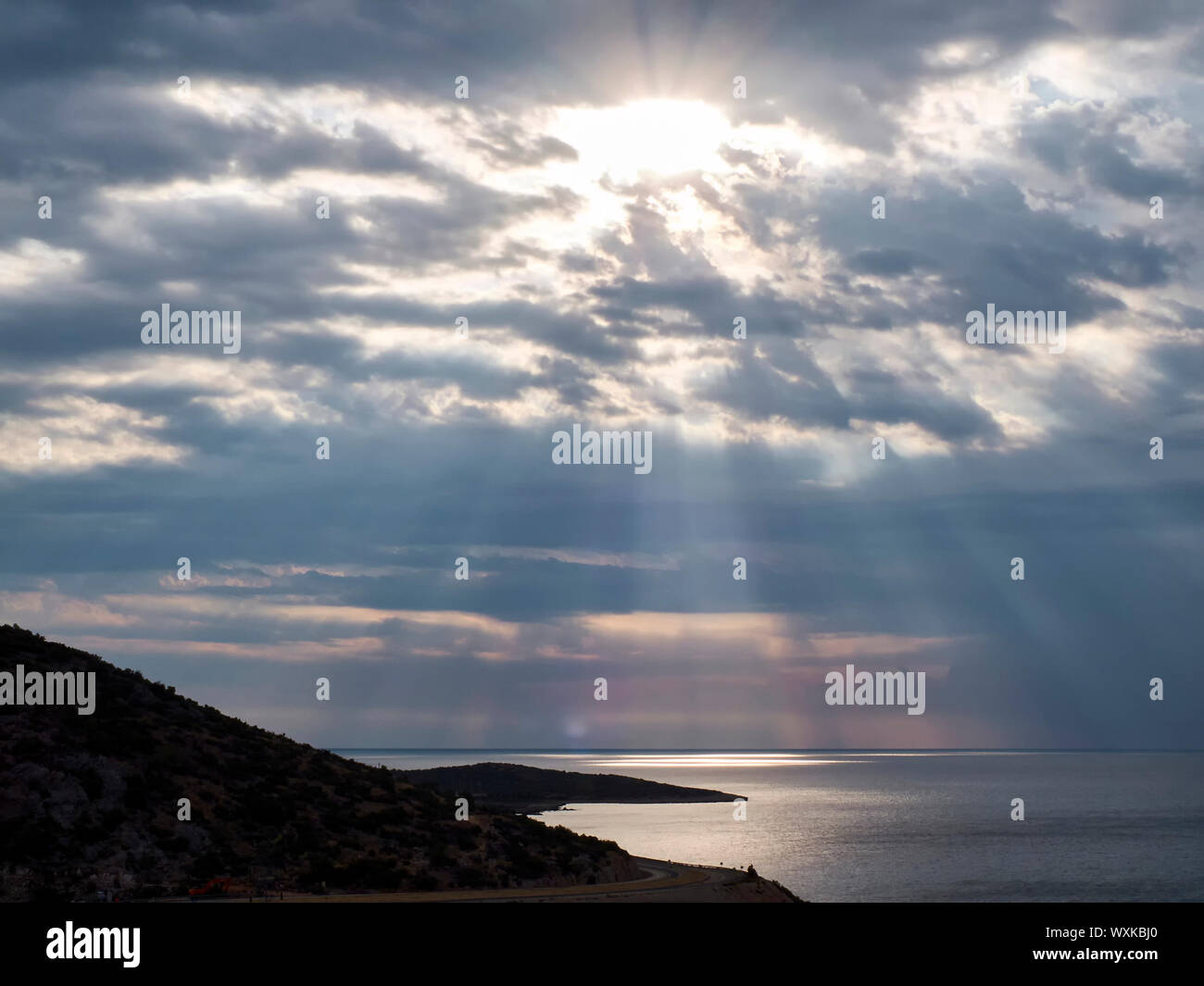 Raggi di sole rompere attraverso le nuvole alla superficie del mare. Strada tortuosa in mattinata. Foto Stock