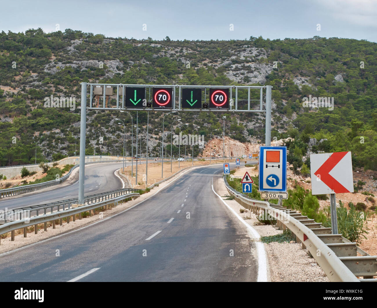 Strada asfaltata con molti dei cartelli stradali e arco in metallo con frecce di direzione e il limite massimo di velocità di segni. Foto Stock