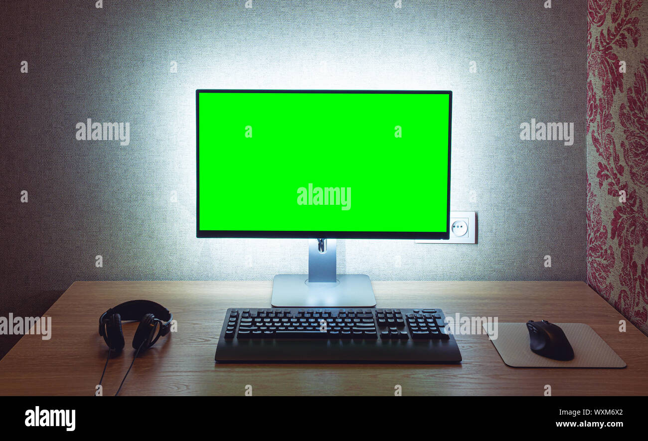 Vuoto monitor Chroma Key con tastiera e mouse con retroilluminazione oltre il muro grigio in dark room Foto Stock