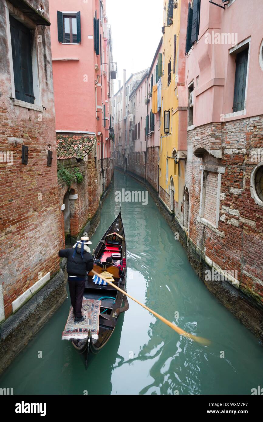 Un gondoliere porta i turisti su un giro in gondola in una tranquilla stretto canale attraverso Venezia in inverno Foto Stock