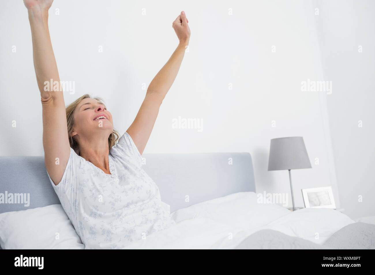 Ben riposati donna bionda stretching nel letto e sorridente in camera da letto a casa Foto Stock