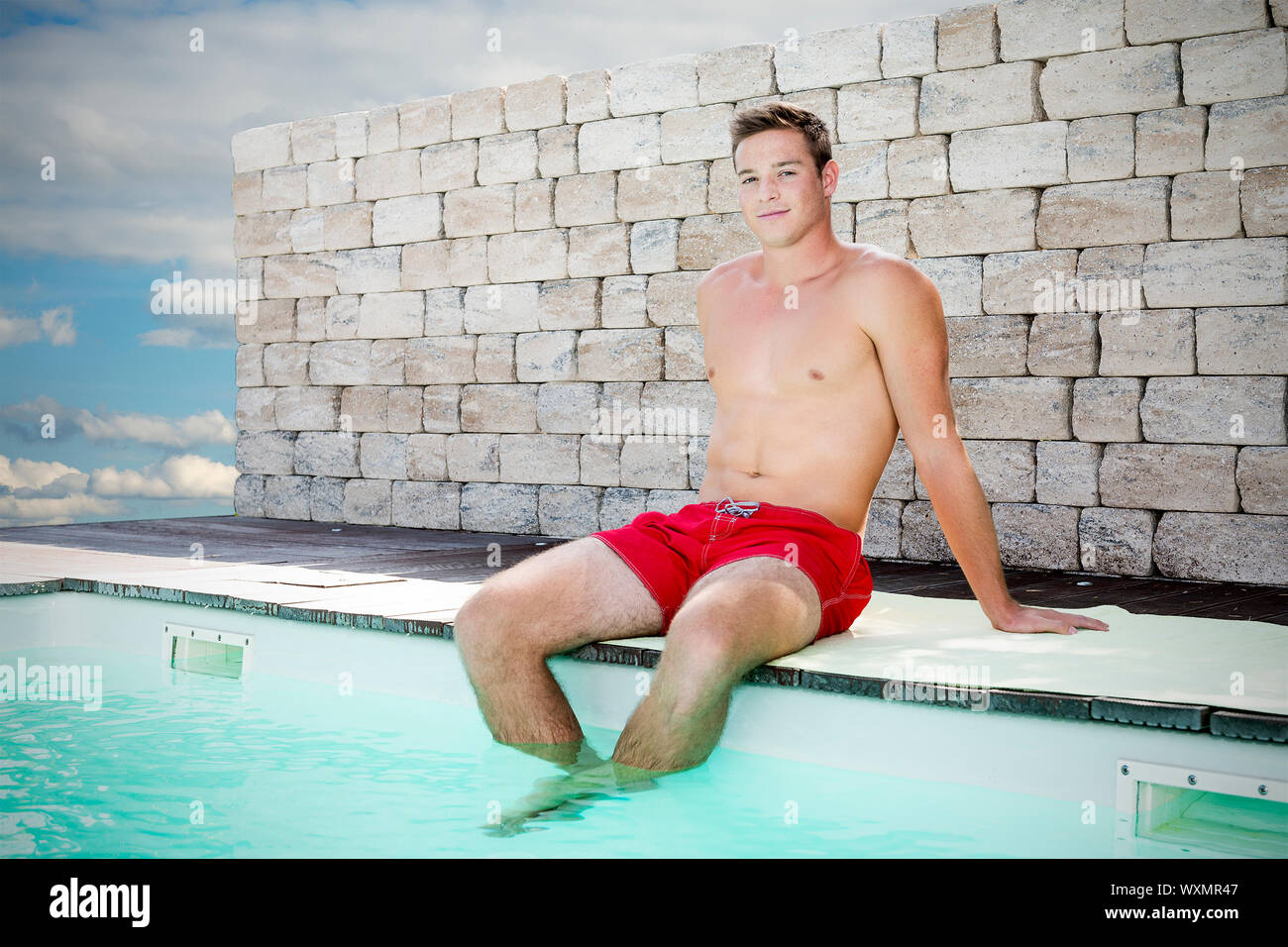 Giovane uomo bello seduto sul bordo di una piscina con pantaloncini corti  Foto stock - Alamy