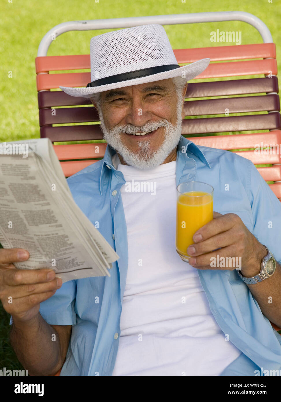 Senior uomo in Prato sedia con giornali e succo di arancia Foto Stock