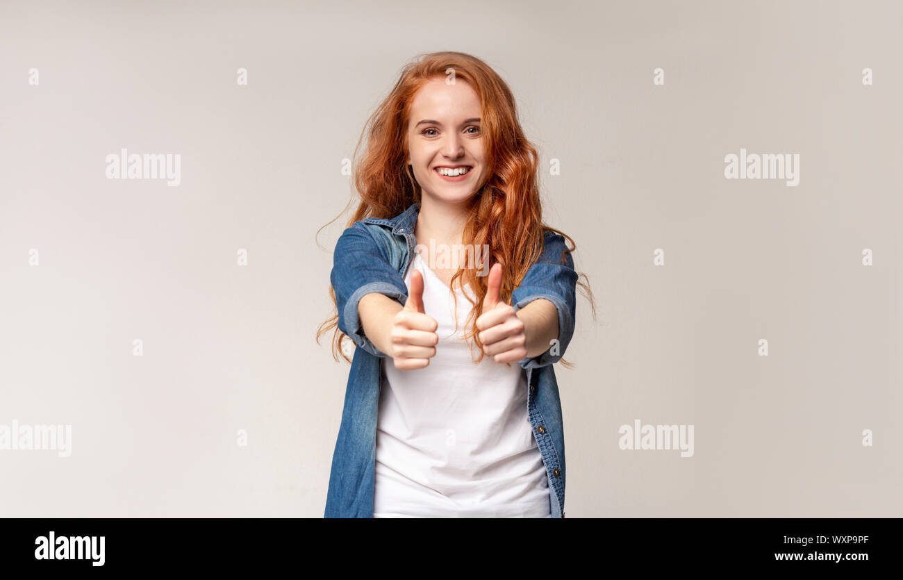 Allegro giovane ragazza redhead che mostra il pollice in alto Foto Stock