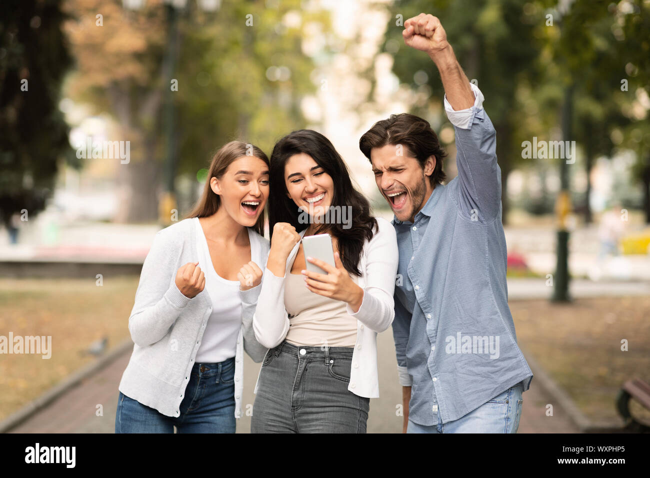 Tre amici leggere grande messaggio sul telefono cellulare in posizione di parcheggio Foto Stock