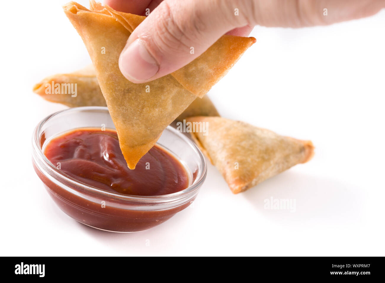 Mano con samosa immersione in salsa agrodolce isolati su sfondo bianco. Tradizionale cibo indiano Foto Stock