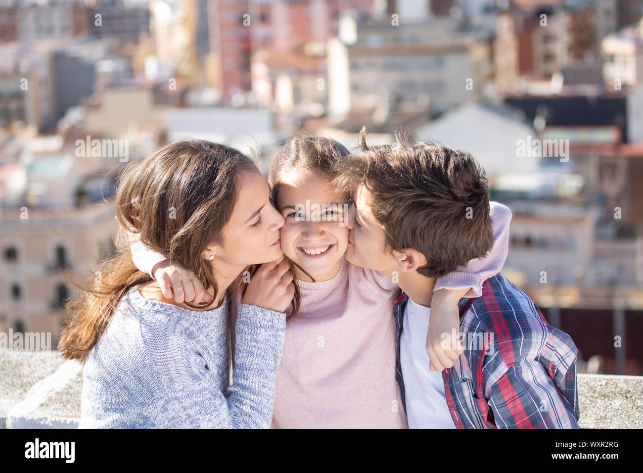 Dos hermanos besando a la vez un su hermana pequeña en la azotea Foto Stock