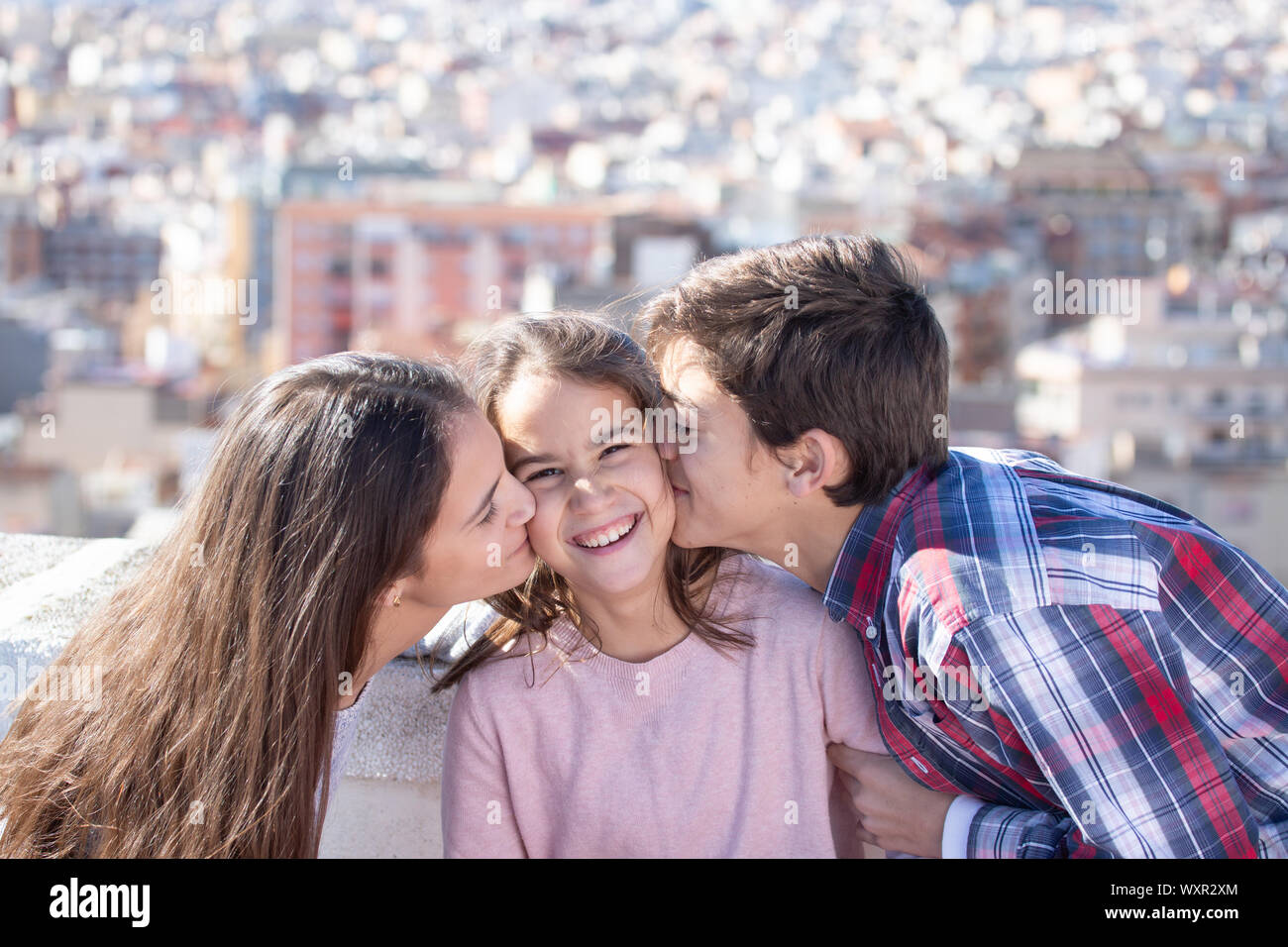 Dos hermanos besando a la vez un su hermana pequeña en la azotea Foto Stock