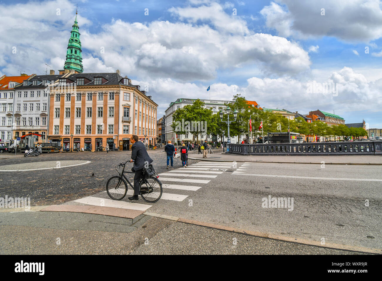 Un imprenditore su una bicicletta attende a un incrocio nel centro urbano di Copenhagen DANIMARCA come San Nicola di Clock Tower di telai a distanza Foto Stock