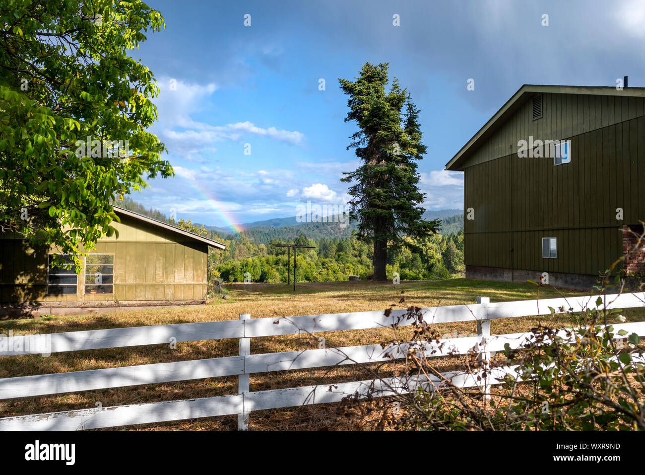 Un arcobaleno è visibile tra una casa e fienile vicino Cataldo, Idaho, tra le montagne della Valle d'argento, Stati Uniti. Foto Stock