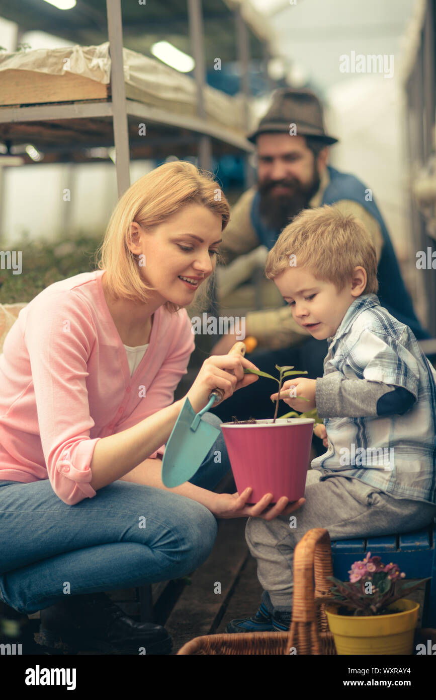 La mamma che mostra il suo figlio foglie di piccolo fiore rosa caldo pot tenendo premuto il giardinaggio vanga. La famiglia felice di lavorare insieme in serra. Foto Stock