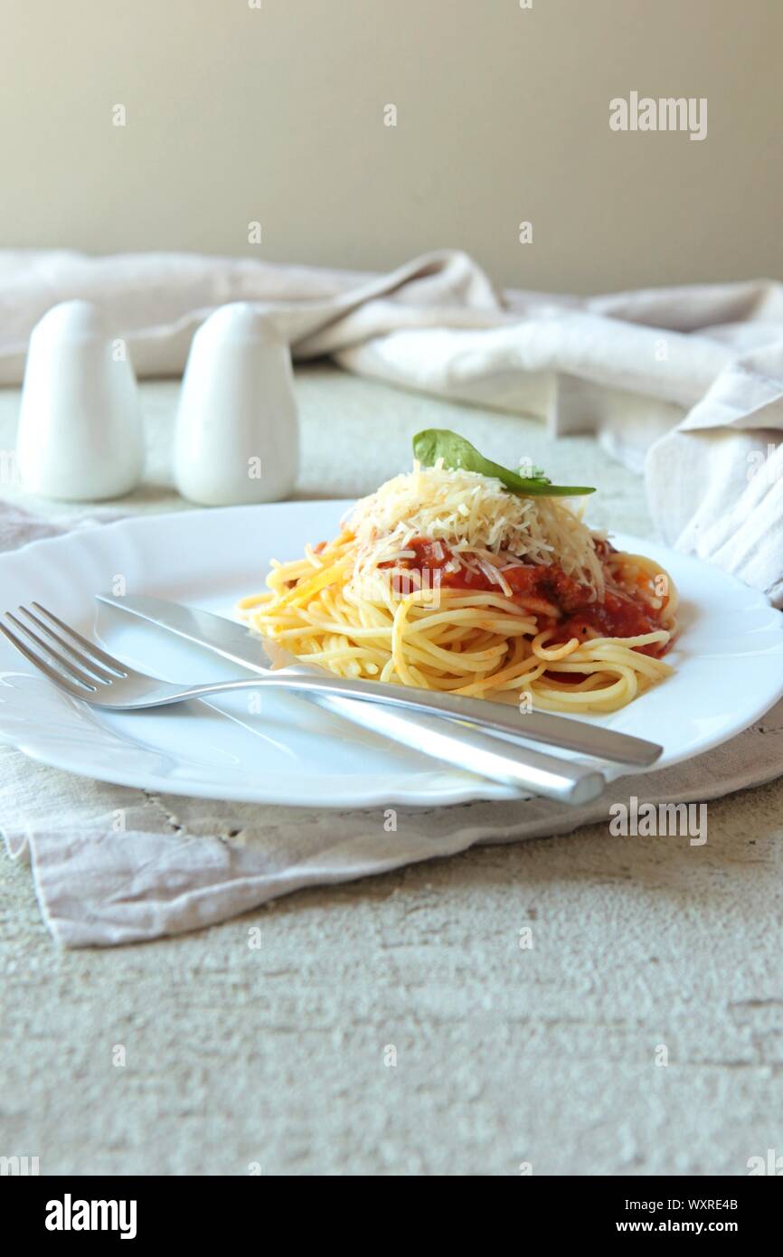 Pasta Fettuccine bolognese con salsa di pomodoro sulla piastra bianca. Carlic e il sale e i pomodori su un sfondo di calcestruzzo con tovaglioli di lino. Foto Stock