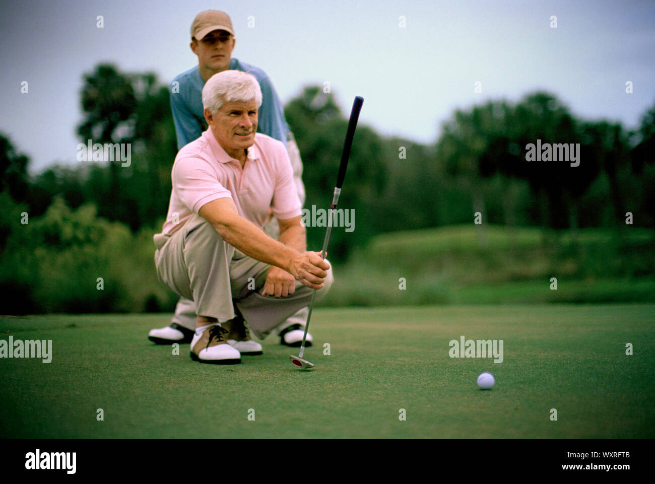 Senior uomo accovacciato mentre allineando il suo prossimo colpo su un campo da golf. Foto Stock