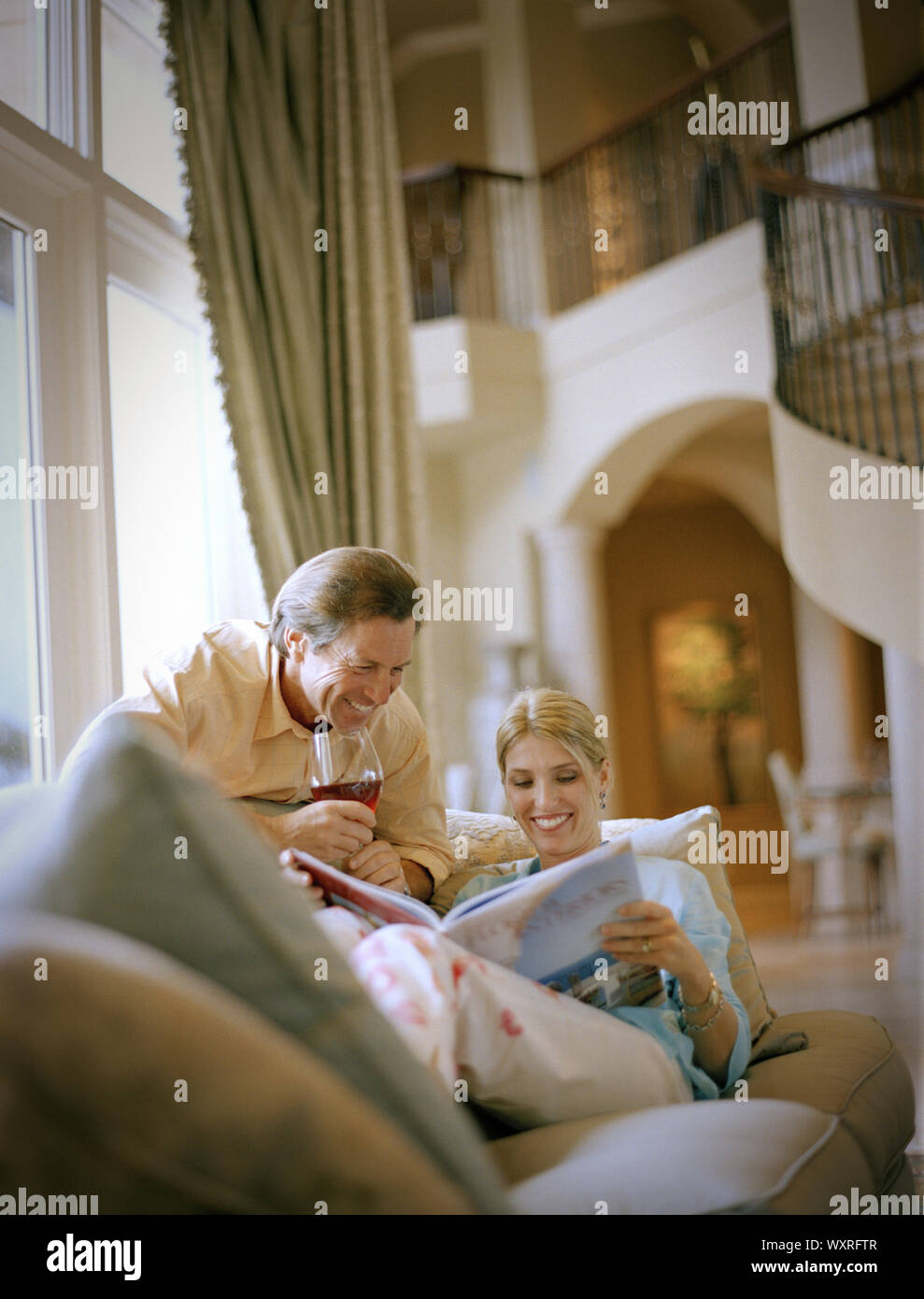 Ritratto di felice coppia sorridente durante la lettura di un libro nel loro salotto. Foto Stock
