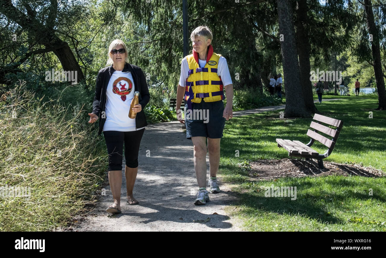 Due donne mature a piedi attraverso il parco. Uno di loro indossa un giubbotto di sicurezza. Foto Stock