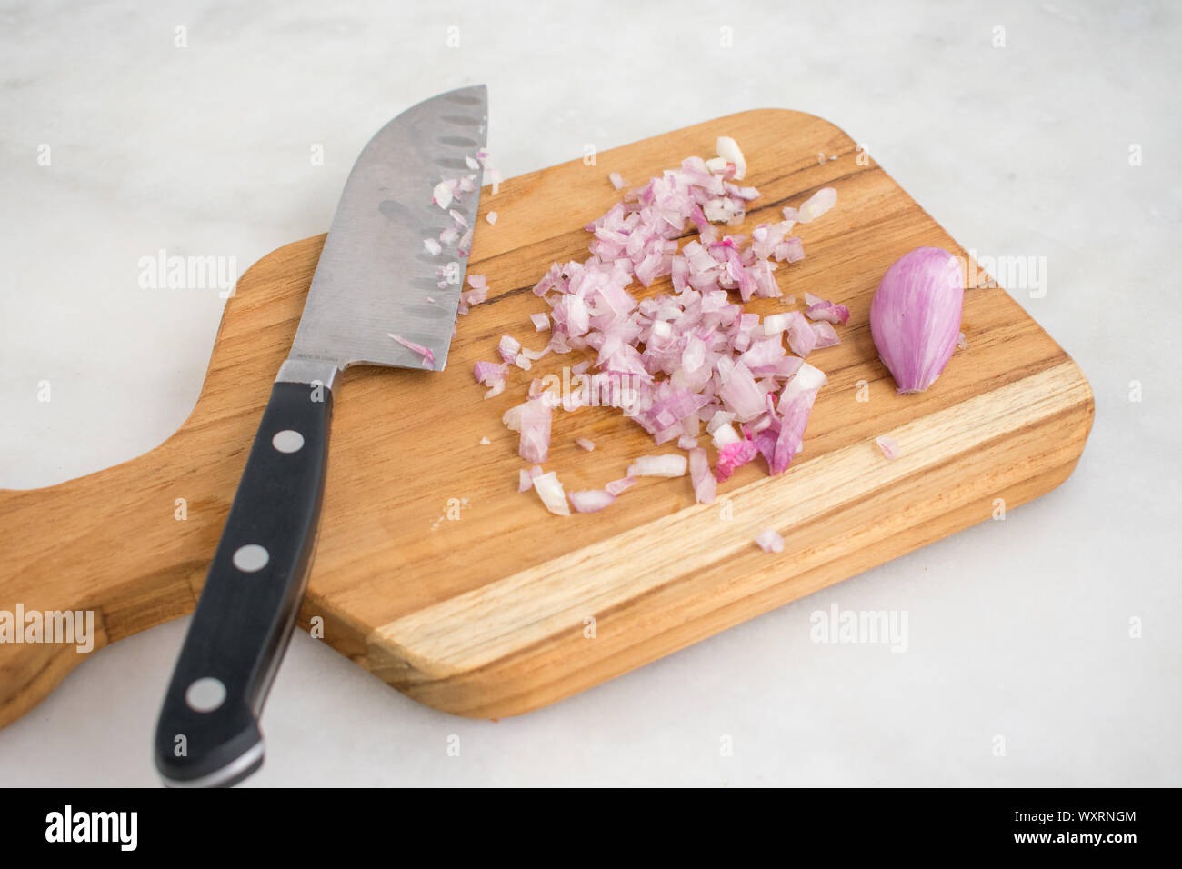 Scalogno tritato su un taglio di legno Scheda: uno scalogno tritato con un chiodo di garofano intero su un legno tagliere con un coltello da cucina. Foto Stock