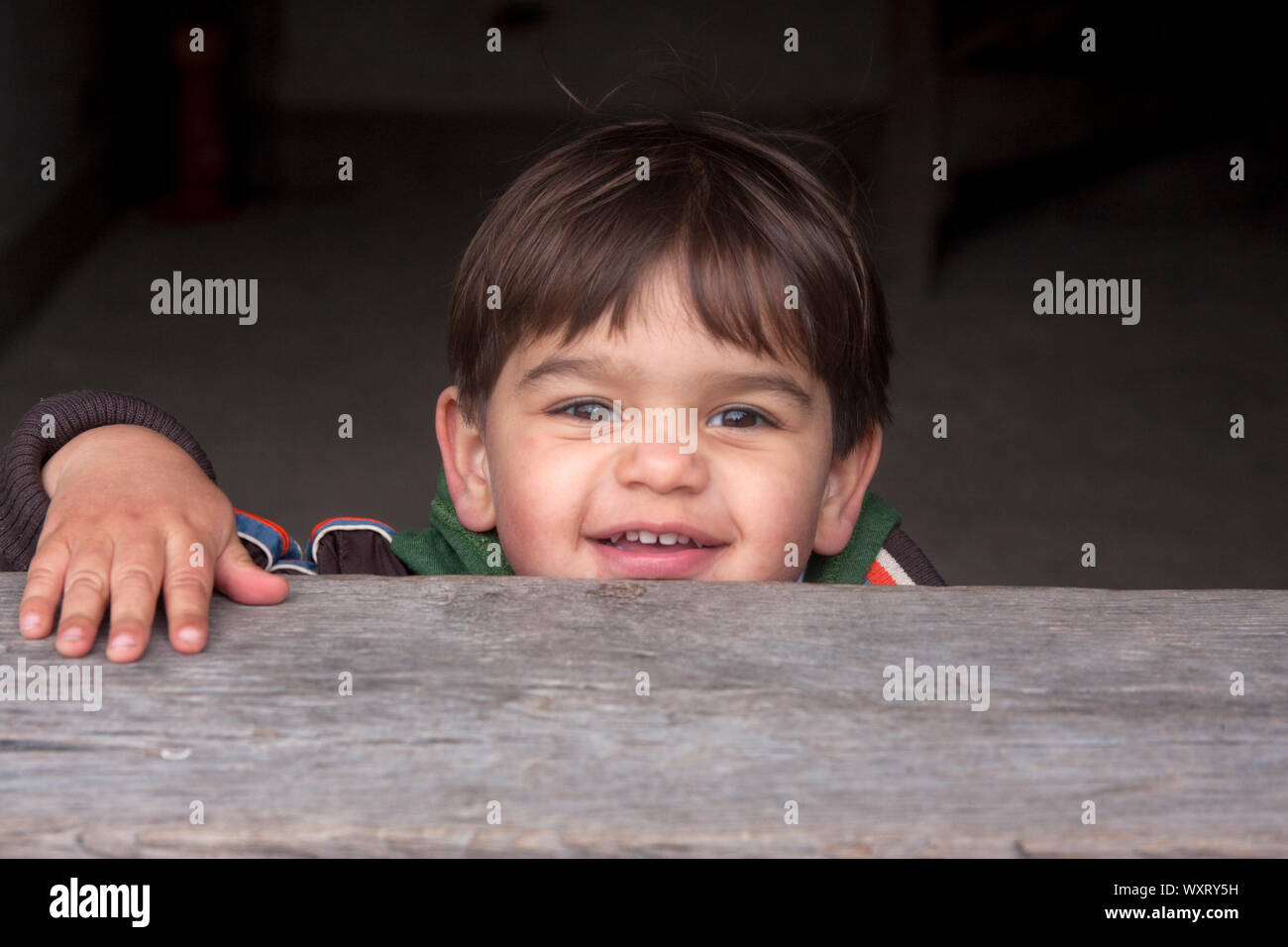 Happy little boy il peering su legno del telaio della porta Foto Stock