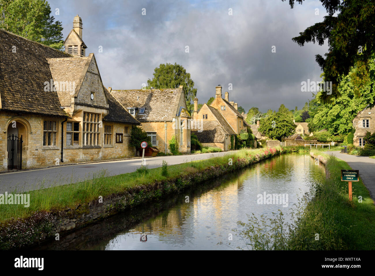 Sole di mattina su giallo Cotswold edifici di pietra calcarea di macellazione inferiore sul fiume occhio con le nuvole scure Gloucestershire in Inghilterra Foto Stock