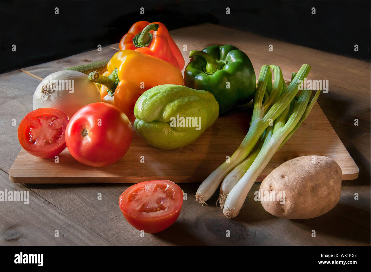 Verdure come peperoni pomodoro aglio potatoe su un tagliere di legno, come parte della vita ancora la fotografia o la scure della fotografia di cibo con backgro nero Foto Stock
