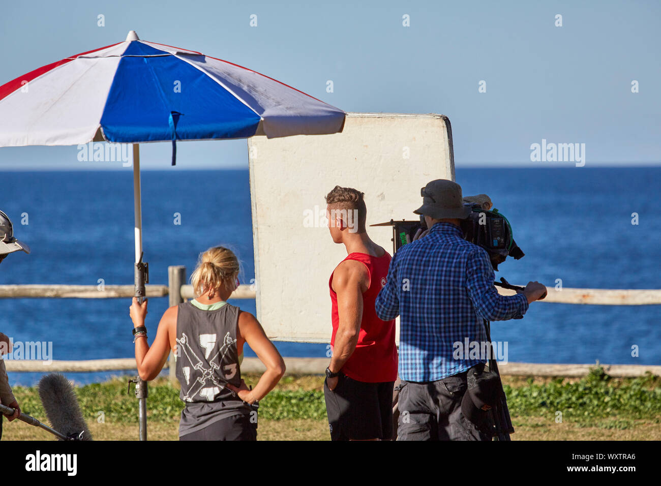 Attori e troupe tra cui un operatore della telecamera le riprese di una scena esterna di Home & Away programma televisivo a Palm Beach, Nuovo Galles del Sud, Australia Foto Stock