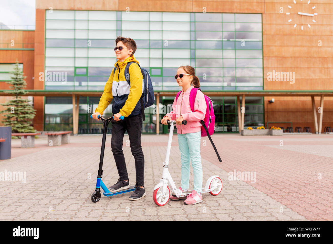 Istruzione, infanzia e concetto di persone - scuola di felici i bambini con zaini scooter equitazione all'aperto Foto Stock