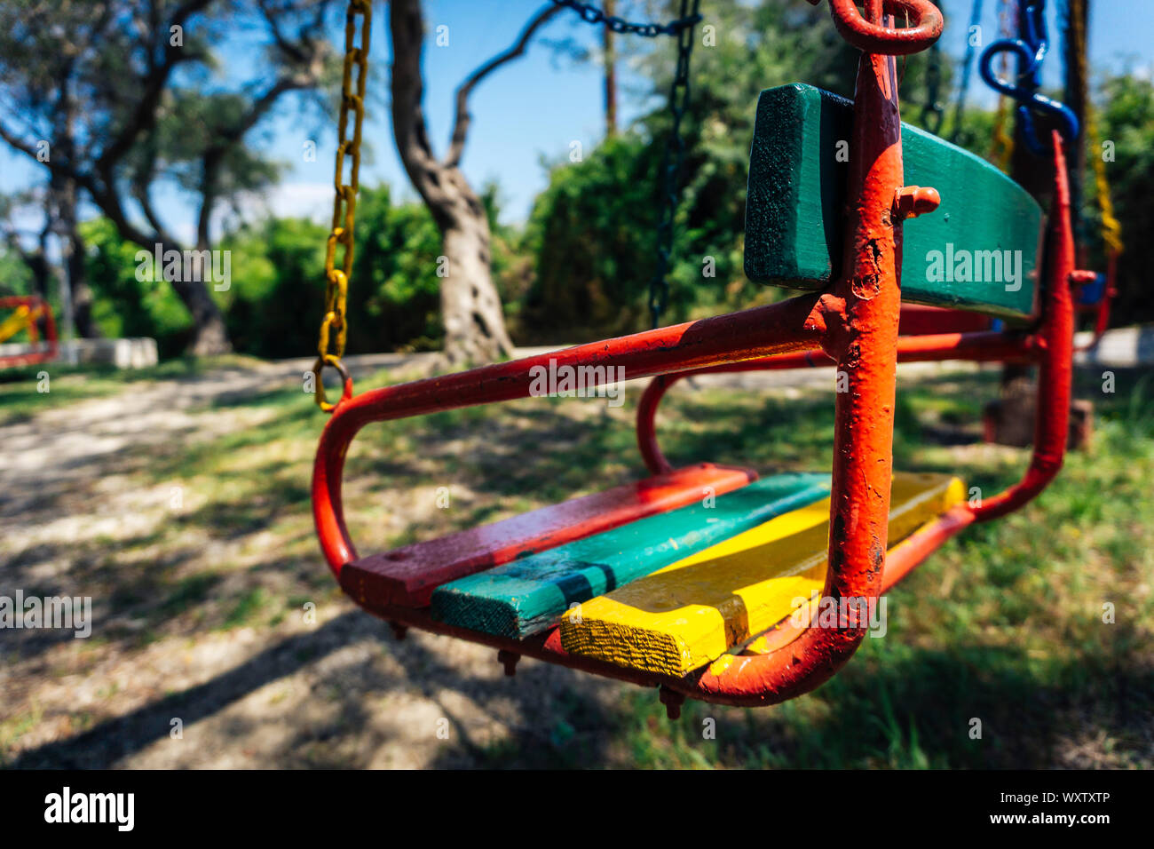 Primo piano della sede di un bambino swing con la vernice scheggiature e in background con vecchi alberi Foto Stock