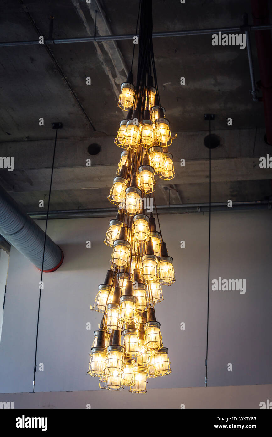 Un gruppo di lampade industriali con giallo lampadine appesa in modo decorativo come lampade bundle su una superficie in calcestruzzo con area per la pubblicità Foto Stock