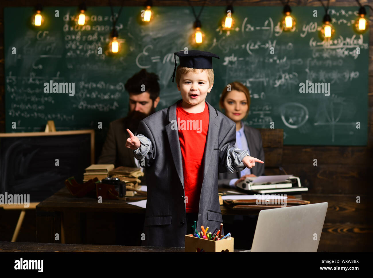 Insegnante moderno hipster iscritto sulla grande lavagna con formula di per la matematica. Gli studenti universitari che studiano con libri in biblioteca. Piuttosto insegnante aiutando la pupilla ho Foto Stock