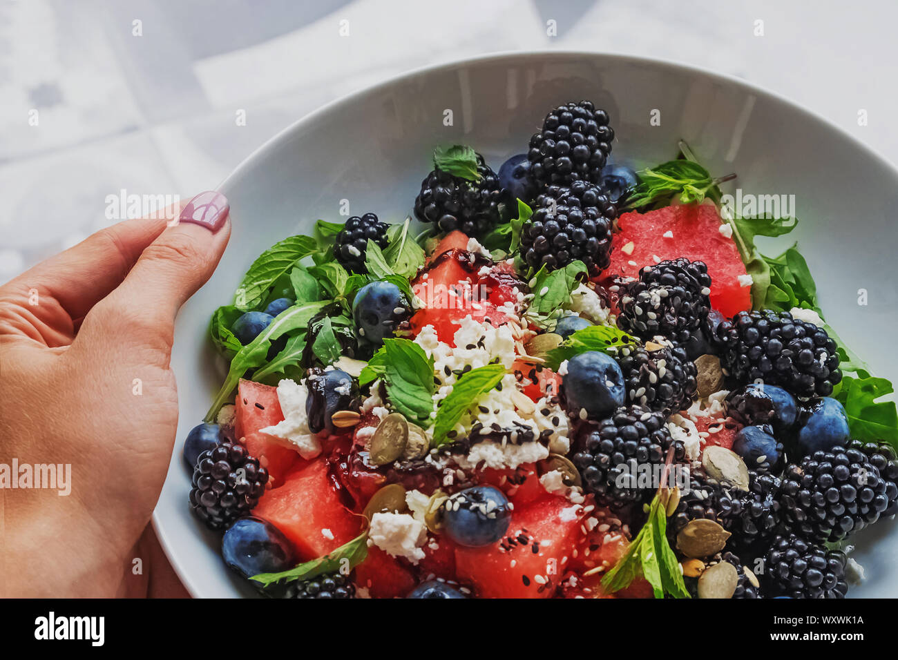 Donna di mano che tiene una piastra con una deliziosa insalata con cocomero, rucola, frutti di bosco e aceto balsamico condimento Foto Stock
