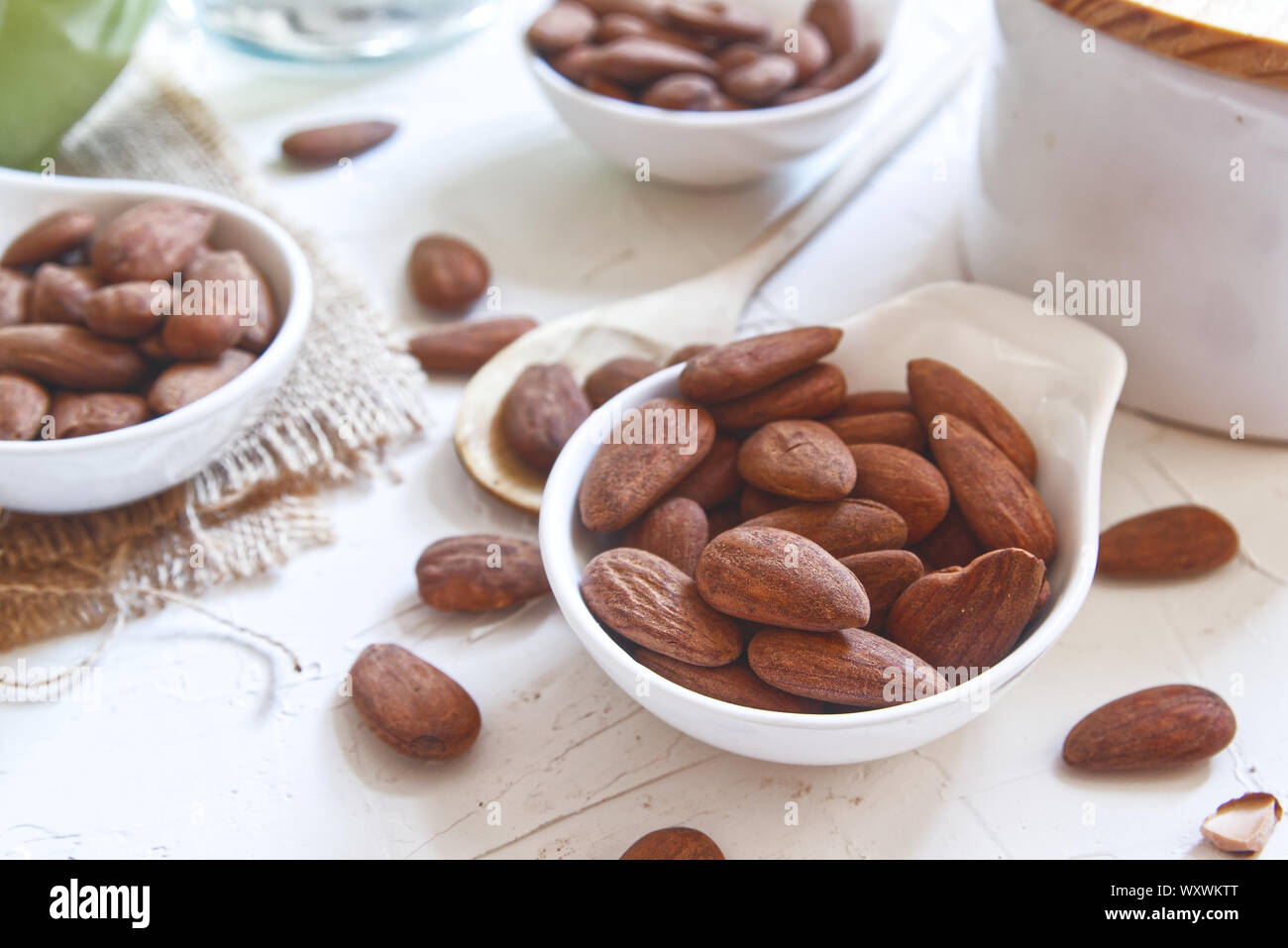 Brown mandorle tostate servito in una ciotola su una bianca tavolo in legno di una cucina rustica. Le sementi e gli ingredienti per la cucina casalinga. Foto Stock