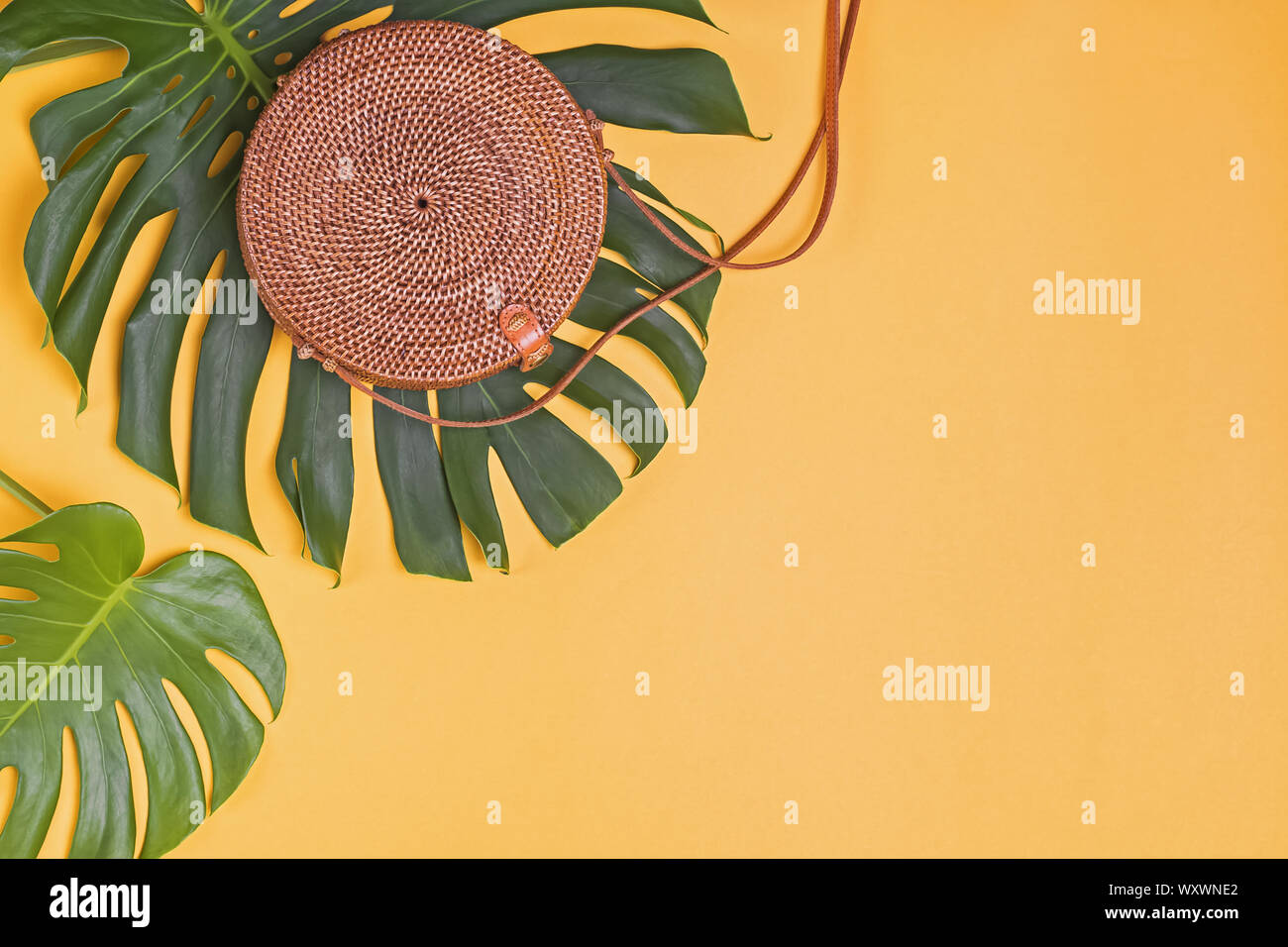Round alla moda eco sacco da rattang giacente su foglie di sul grande impianto di monstera , vista superiore Foto Stock