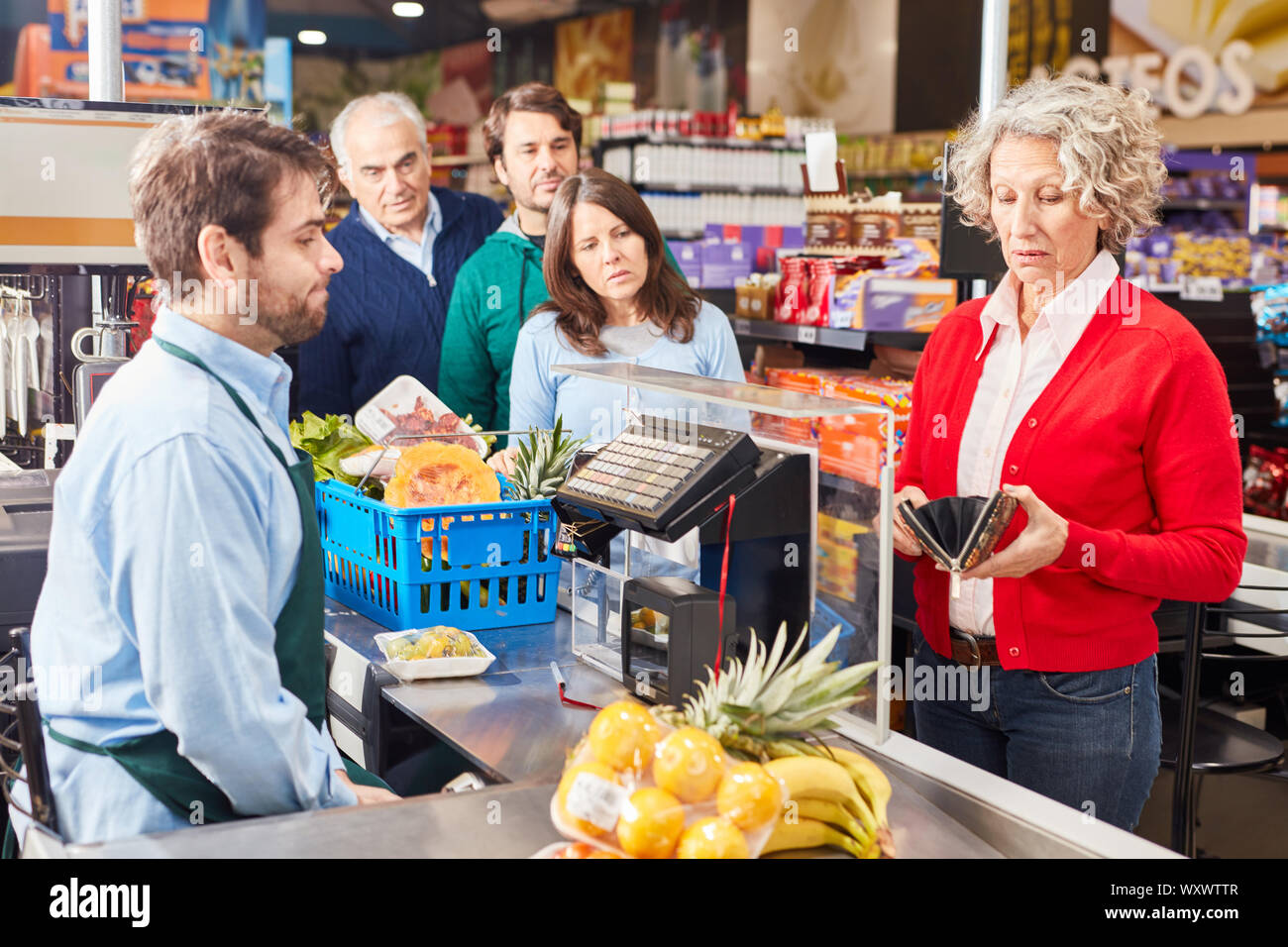 Senior donna il pagamento alla cassa del supermercato guarda nel suo portafoglio Foto Stock