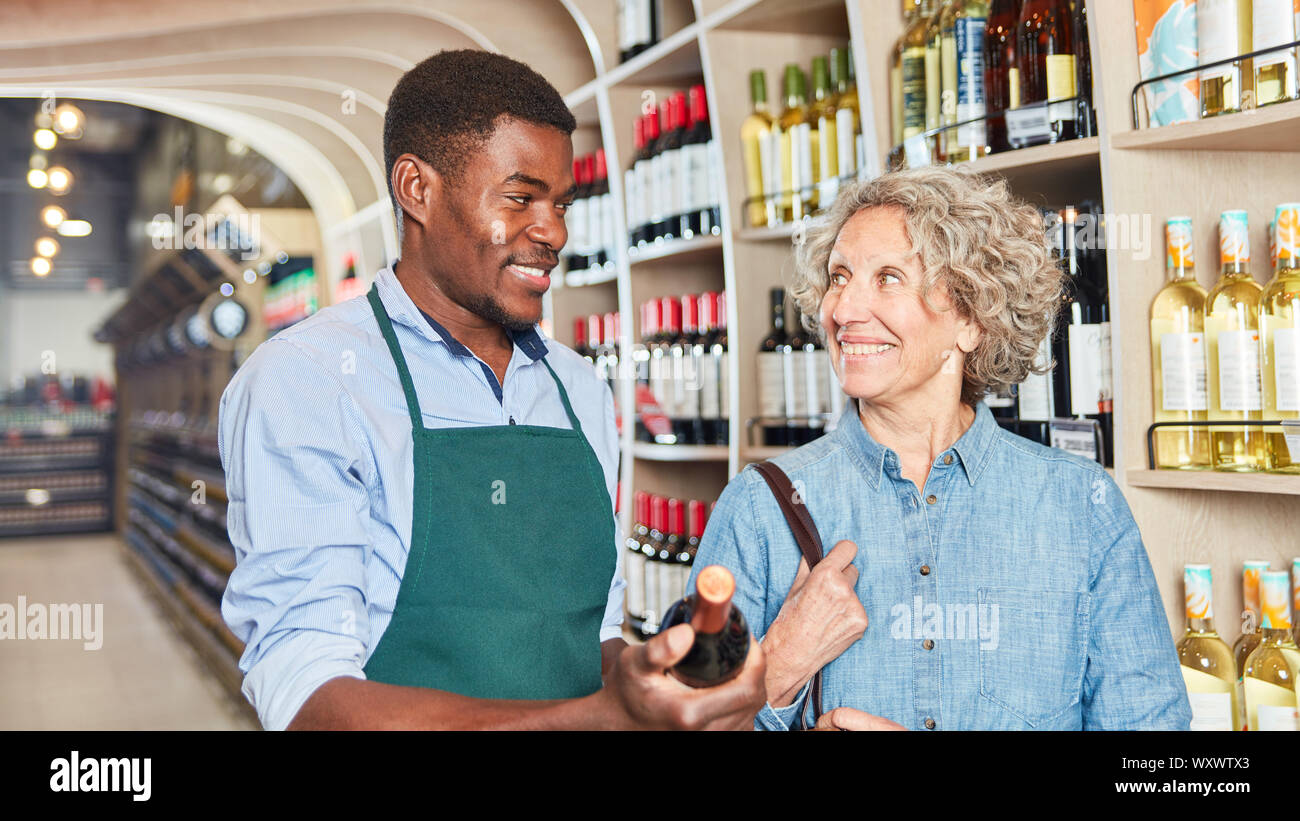 Il cliente riceve consigli sugli acquisti di vino rosso dal venditore africana Foto Stock