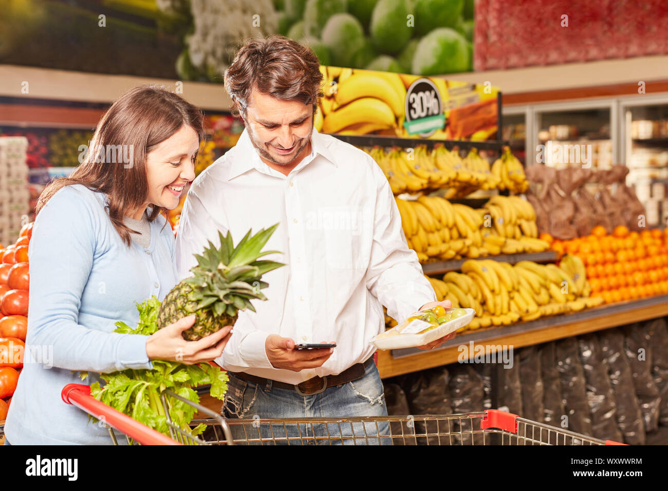 Coppia giovane acquisto di ananas utilizza uno smartphone app per il confronto dei prezzi Foto Stock