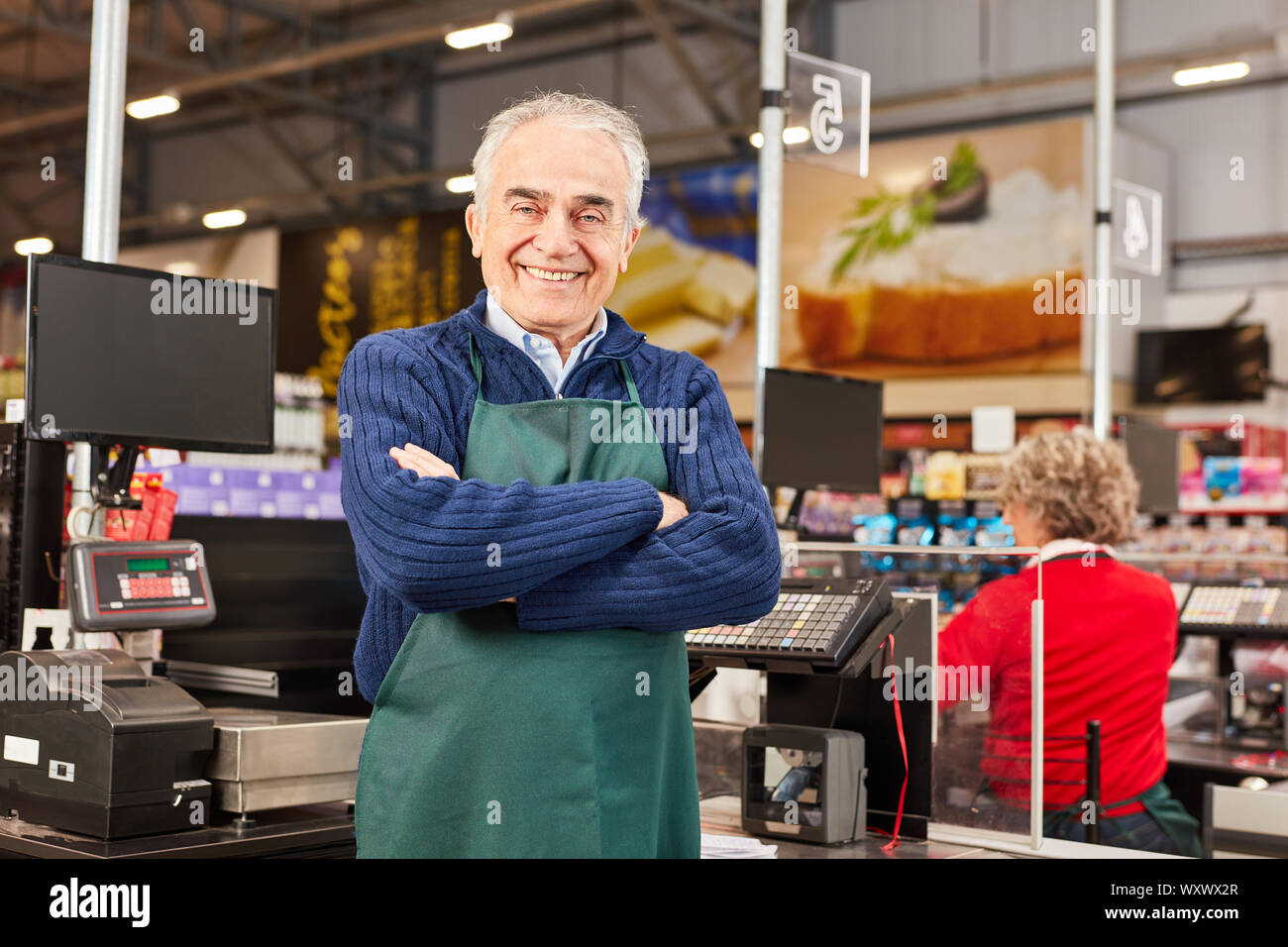 Sorridente come senior market manager con bracci incrociati nel supermercato Foto Stock