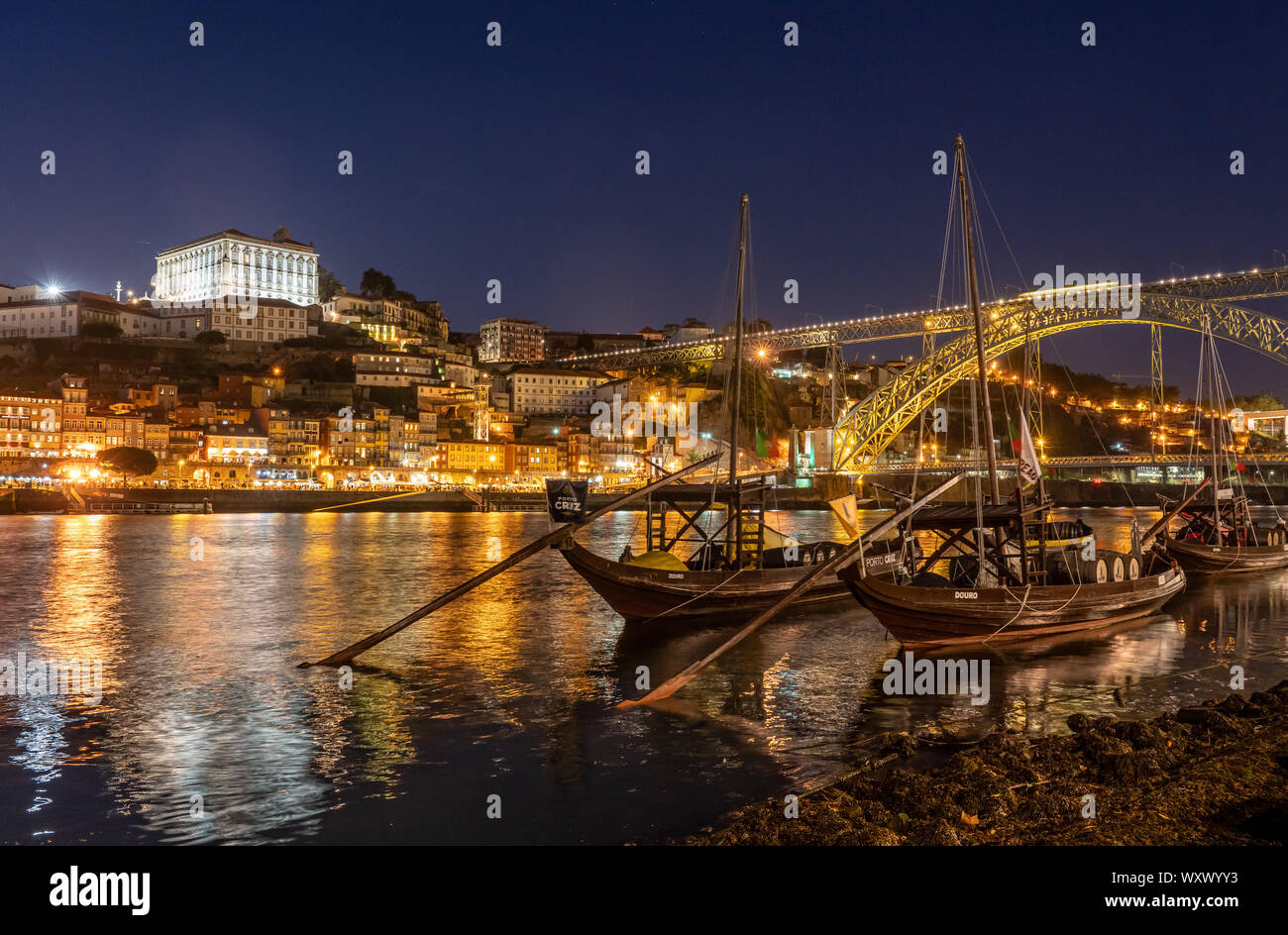 Rabelo barche usate per il trasporto dal porto di Porto in Portogallo con un panorama dello skyline della città vecchia di notte con luci che riflettono nel fiume Foto Stock