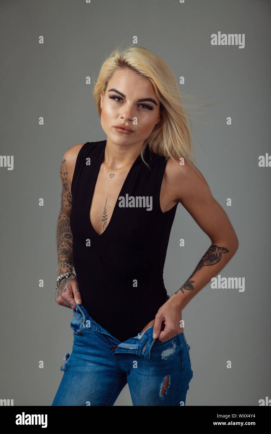 Una giovane e bella donna con tatuaggi indossando un body senza maniche e jeans strappati Foto Stock
