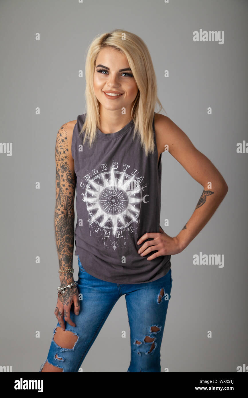 Una giovane e bella donna con tatuaggi indossare una T-shirt senza maniche e jeans strappati Foto Stock