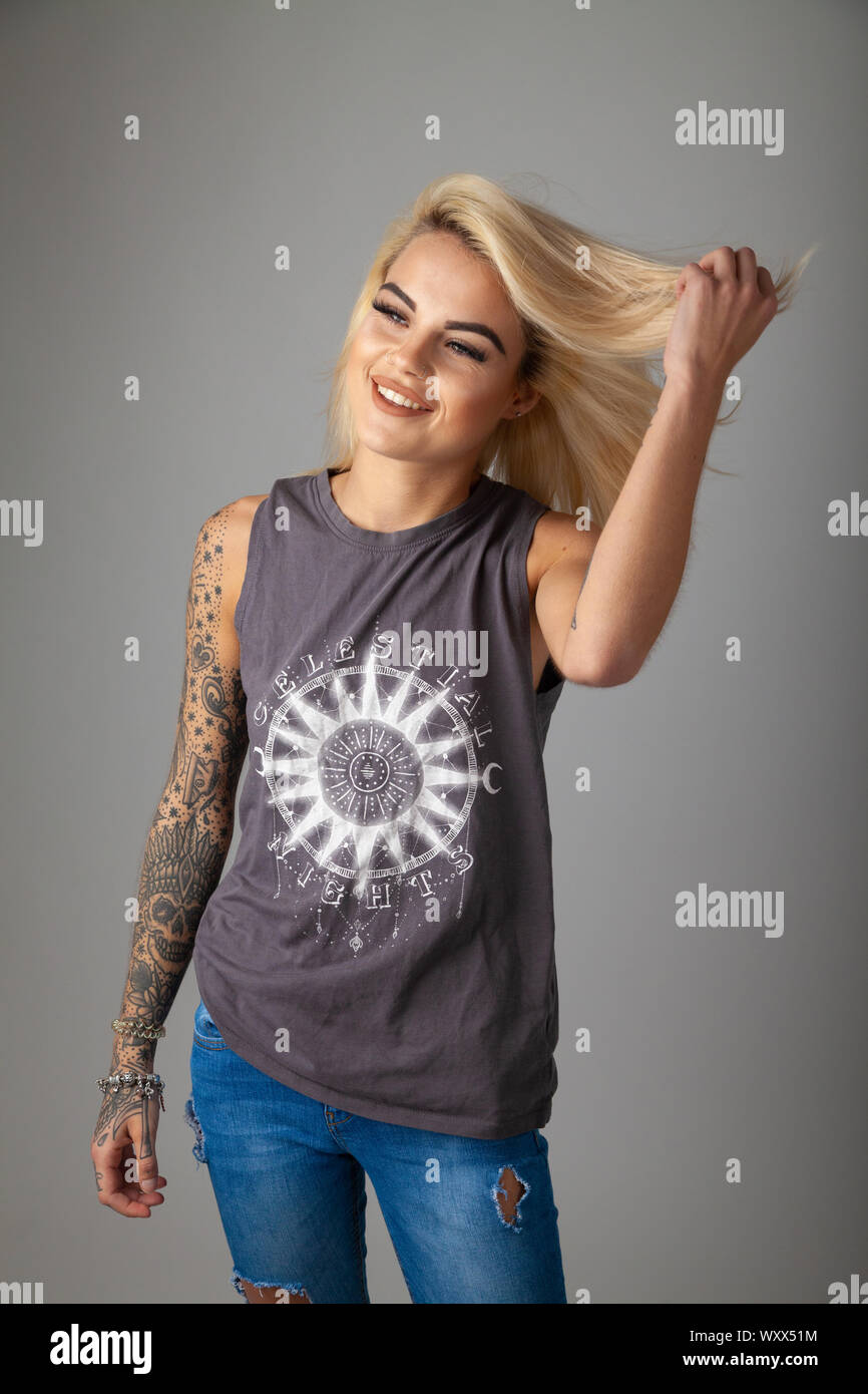 Una giovane e bella donna con tatuaggi indossare una T-shirt senza maniche e jeans strappati Foto Stock