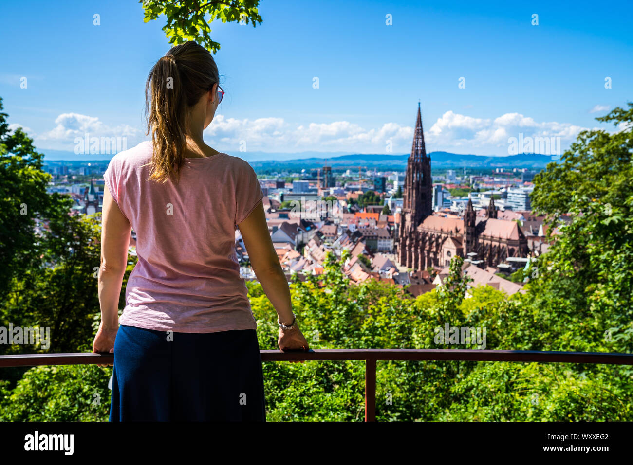 Germania, biondo giovane bella donna in piedi sopra città Freiburg im Breisgau skyline e la città vecchia con la famosa cattedrale minster in estate Foto Stock